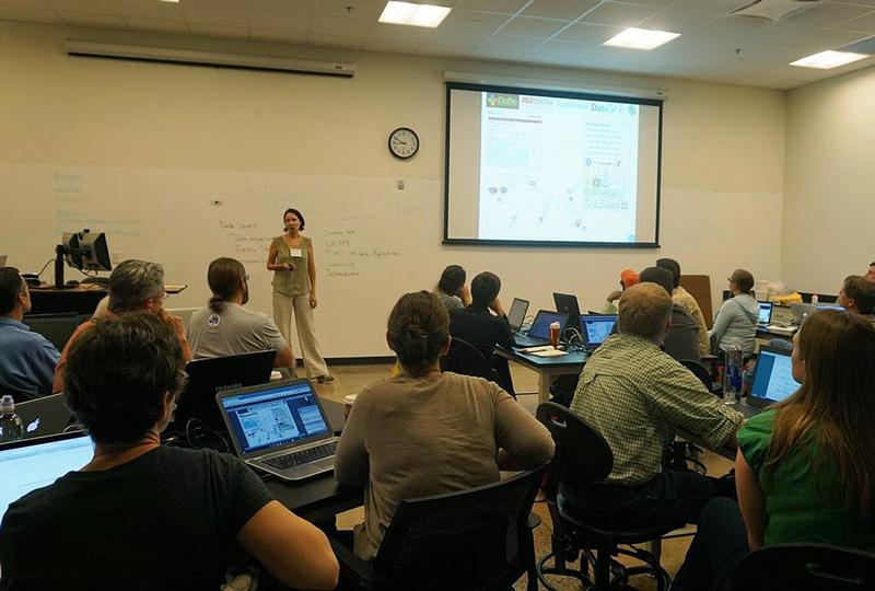 Group of people in a classroom with laptops watching presenter