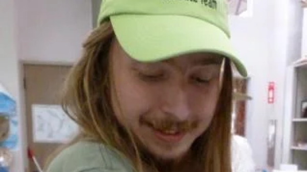 Young man with long hair and green hat looking down