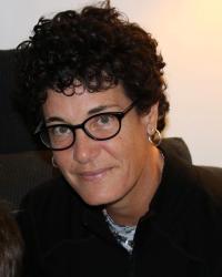 Woman with short, dark curly hair wearing glasses and black shirt