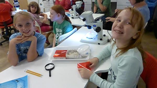 Kids sitting at tables with microscopes